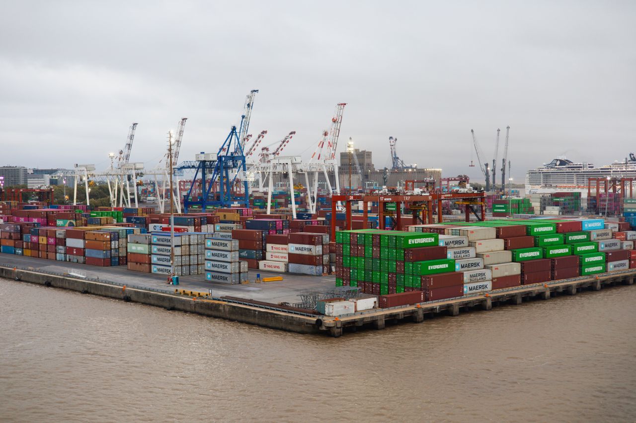 About A bustling shipping port with stacked cargo containers and cranes under overcast skies.
